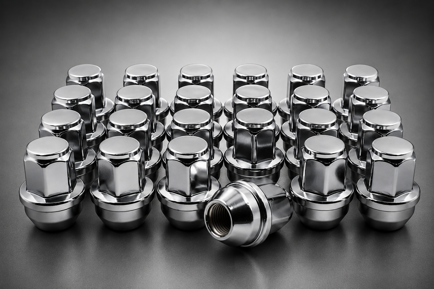 A set of shiny chrome lug nuts arranged in rows on a dark gray studio background, with one nut lying on its side in front.
