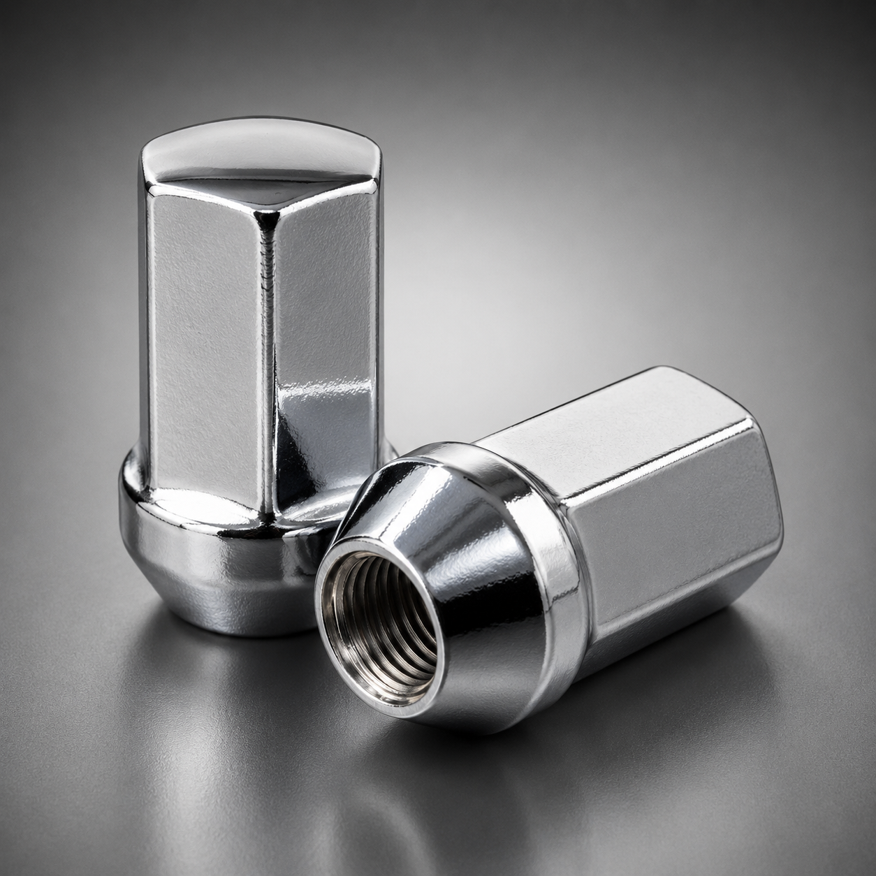 Two polished chrome metal lug nuts on a dark gray gradient background, one standing upright and the other lying on its side showing the threaded interior.