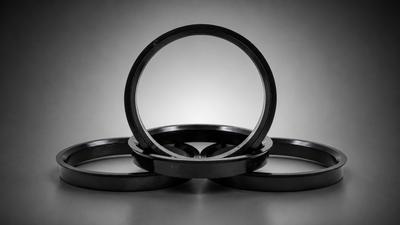 Four black hub centric rings arranged in a stacked, overlapping display on a dark gray gradient studio background.